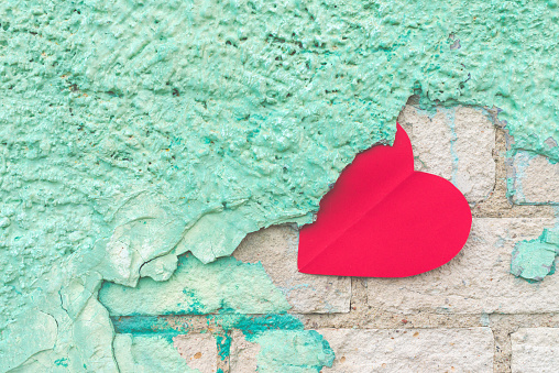 Valentine day background with red paper heart on a rustic green crumbling wall.the heart is stuck on the stucco.