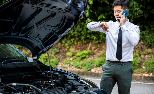 Distraught businessman waiting for towing service after car crash. Horizontal photo of elegant man in suit sitting on highway, looking despair and headache. Concept for insurance and transportation.