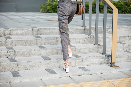 A businesswoman in a modern suit is captured in a determined ascent on city stairs. Her black shoe-clad foot is the embodiment of relentless effort, achievement, and success in the business world.