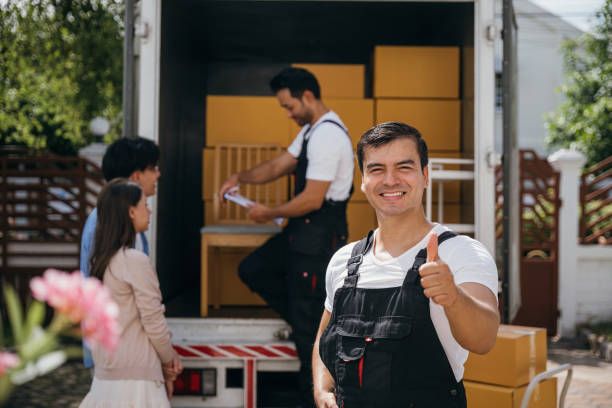 Um motorista sorridente capturado em um retrato descarrega caixas em uma nova casa de um caminhão. Esses trabalhadores da empresa de remoção garantem uma movimentação eficiente e felicidade. Conceito de dia em movimento - foto de acervo