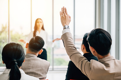 In a seminar classroom, a large group actively participates in the discussion, with raised hands indicating their engagement. The answers reside within this dynamic conference audience.