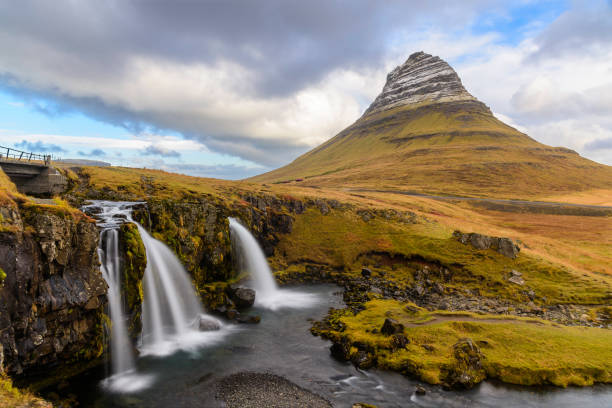 Kirkjufell and Kirkjufellsfoss, Snæfellsnes Peninsula, Iceland Kirkjufell is a 463 m high mountain on the north coast of Iceland's Snæfellsnes peninsula, near the town of Grundarfjörður. The name Kirkjufell means Church Mountain as it is considered to resemble a church.
It is claimed to be the most photographed mountain in the country due to its dramatic formation and perfect coastal location.
Within walking distance from Kirkjufell is the serene and perfectly located waterfall Kirkjufellsfoss, or Church Mountain Falls. Despite its relatively diminutive height, Kirkjufellsfoss three steps, gentle flow, and dramatic differences between seasons make it as impressive as some of Icelands larger waterfalls.
Kirkjufellsfoss, Kirkjufell, Grundarfjörður, Snæfellsnes, Iceland, Europe. peninsula stock pictures, royalty-free photos & images