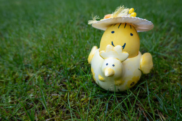 yellow colored easter egg smile hat in the chicken shape ceramic holder on green background. Happy Easter. He is risen
