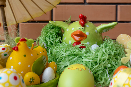 Happy easter decoration. Composition made of colorful dyed easter eggs near ceramic chicken figure in a straw nest basket