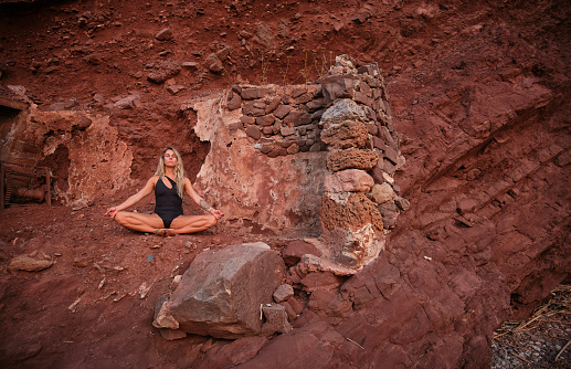 Full body of slim woman in Bound Angle pose meditating with eyes closed while sitting on mountain cliff
