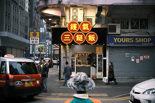 People on a street in Mongkok district, Kowloon peninsula. Red Taxi passing by.