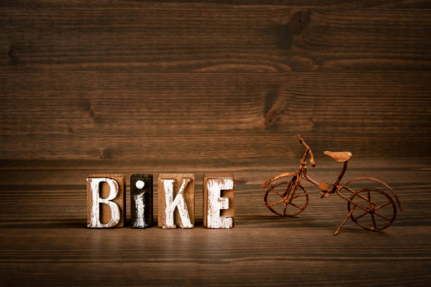 BIKE. Text from alphabet blocks and rusty miniature bicycle on wood texture background.