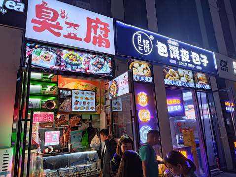 Young people at neon lighten snack shops in Sanlitun Soho shopping complex, an area of the Chaoyang District, Beijing, a popular destination for shopping, dining, and entertainment.