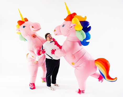 Smiling man having fun with unicorns in rainbow costume of LGBT community symbols in studio against white surface