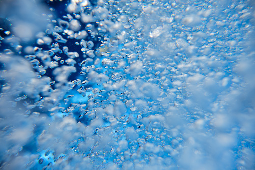 Closeup of many transparent different shaped air bubbles floating deep in clear water