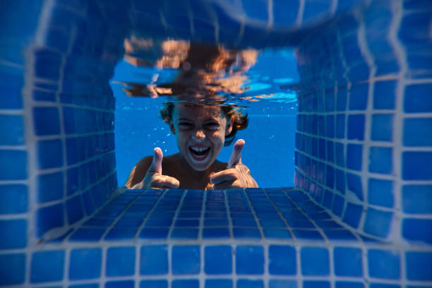 Underwater excited child having fun while swimming in blue pool and looking at camera on weekend summer day