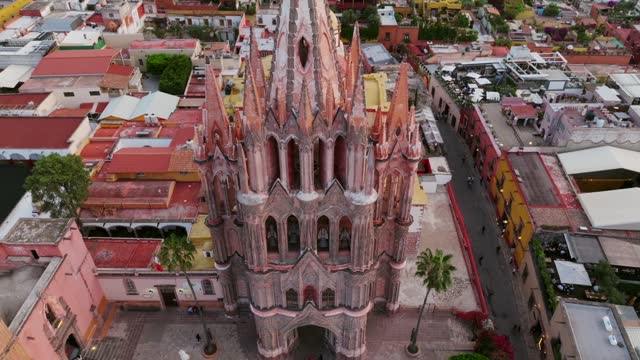 Towering Pink Spire Of Parroquia de San Miguel Arcangel In San Miguel de Allende, Guanajuato, Mexico. aerial pullback, tilt-down