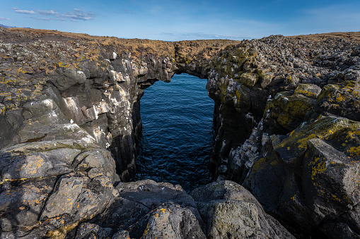 A rock arch above the blue waters of the sea. Iceland