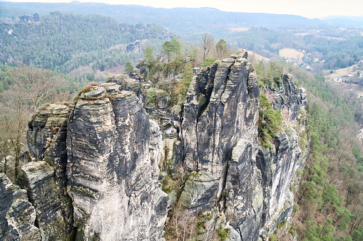 Jagged rocks at the Basteibridge. Wide view over trees and mountains. Dramatic sky. National park in Germany