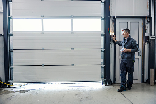 A mechanic is pressing button and opening garage door at the car workshop.