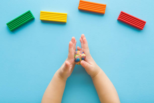 istock Baby boy hands rolling colorful ball from modeling clay on light blue table background. Pastel color. Closeup. Point of view shot. Toddler development. Making shape. Top down view. 2045255543