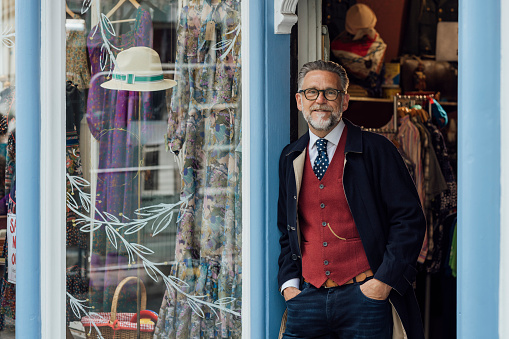 Man dressed formally in a waistcoat and jacket  standing outside of a vintage clothing store. He is smiling looking at the camera with his hands in his pockets. The store is in Durham, Northeast England.