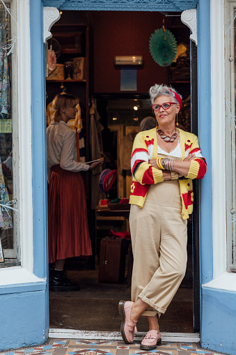 Woman dressed in fun vintage style clothing  standing outside of a vintage clothing store. She is looking away from the camera with her arms crossed. The store is in Durham, Northeast England.