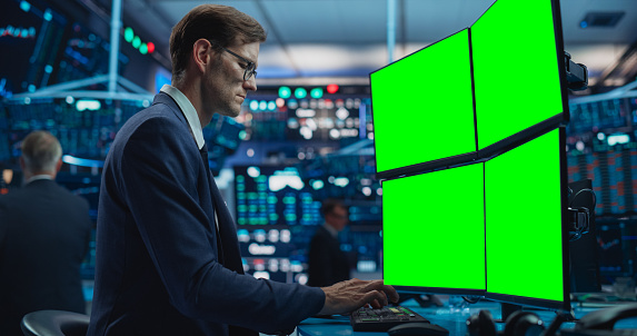 Portrait of Young Handsome Stock Exchange Broker Working on Computer With Green Screen Chromakey On Display, Analyzing Commodities and Exchange Market Charts. Professional Investment Agent in Office
