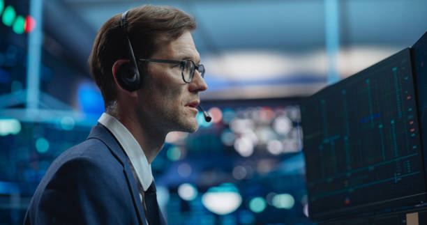 istock Professional Stock Exchange Trader Performing with Serious Focused Expression. Stockbroker Talking with Business Clients on a Call, Working on Computer, Speculating on Buying Shares for Trading 2045282270