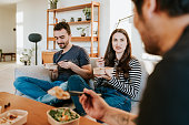 Diverse group of friends gather in a cozy living room, enjoying Asian takeout food together