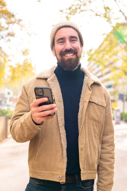 istock Vertical portrait smiling young man is browsing the internet with a smart phone outdoors. 2045302897