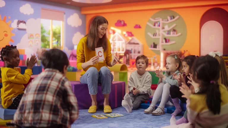 Happy Kindergarten Pedagogue Having a Conversation with Kids, Using Enthusiastic Teaching Methods in a Modern Colorful Kindergarten. Female Educator Stimulating Linguistic and Social Skills
