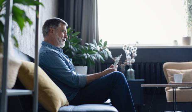 istock Man relaxing at home on a comfortable sofa with his tablet pc reading online with a quiet smile of pleasure 2045310805