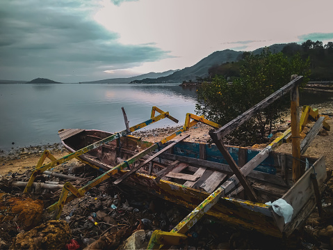 a broken wooden boat on the shore filled with organic and plastic waste