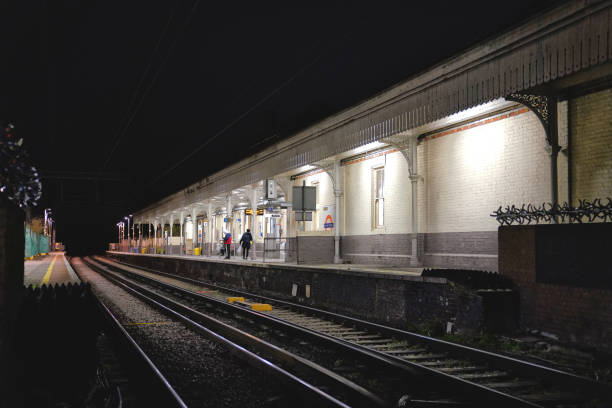 Acton, London Borough of Ealing, West London, England, United Kingdom - February 27 2024: 'Acton Main Line Station' and Acton Central railway station, showcasing the parallel steel rails of the train tracks belonging to both London Overground and Network Rail. A perspective view. Urban subway lights.