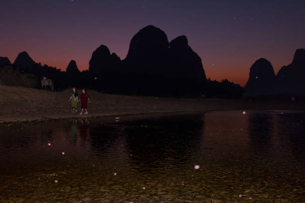 Yangshuo County, Guilin City, Guangxi, China - October 23, 2023: Two tourists are walking along the Li River at dusk