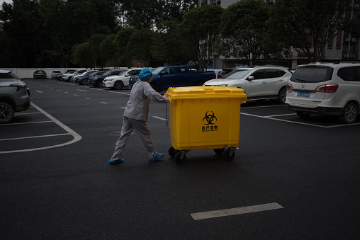 Xing'an County, Guilin City, Guangxi, China - October 26, 2023: An environmental worker is pushing a trolley containing medical waste through the parking lot.