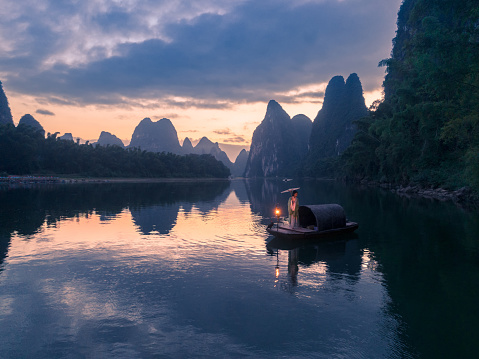 Yangshuo County, Guilin City, Guangxi, China - October 06, 2023: A tourist dressed in Chinese costume is taking photos on the Li River at dawn