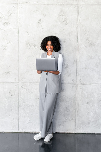 Standing upright with a laptop, this African-American businesswoman's contented expression speaks to the flexibility and mobility of modern work life.