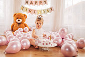 The cute baby girl is sitting on the floor, and touching the 1st birthday cake. Cake smash