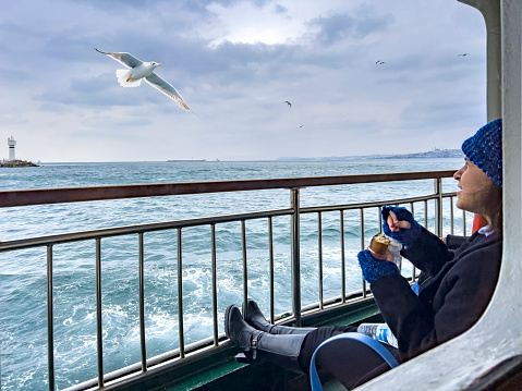 Istanbul, Turkey - 6 March 2022: A local girl feeds bread to seagulls on board a ferry crossing the Bosphorus from the European side of Istanbul to the Asian side. Ferries are a form of public transport popular with locals and tourists.
