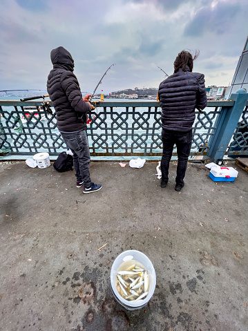 Istanbul, Turkey - 6 March 2022: People fishing on the Galata Bridge on a cold winter's day.