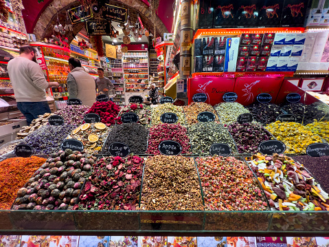 Istanbul, Turkey - March 6, 2022: Front view of an open shop in the spice bazaar, with people inside bargaining for a huge variety of colourful dried herbal teas. Healthy and delicious different flavours