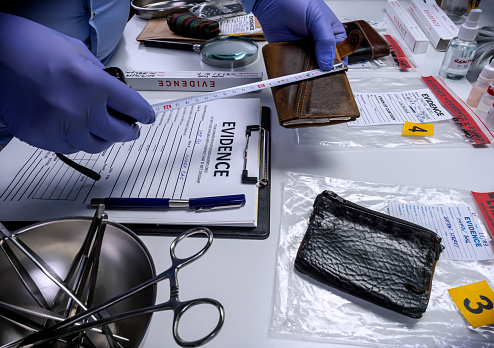 Specialised police officer measures wallet in crime lab, conceptual image