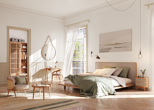 A tranquil, well-lit bedroom featuring a modern aesthetic with a comfortable bed adorned with soft linens. The room is complemented by a stylish wooden wardrobe, a cozy armchair, and a small writing desk, all bathed in natural sunlight filtering through sheer curtains.