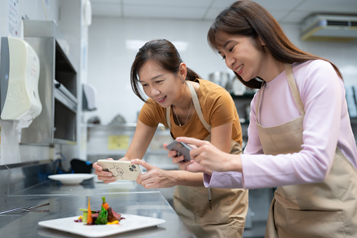 2 female students taking photo for their own prepared dishes with smartphone