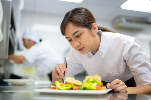 Female chef finalizing garnishes before serving in a commercial kitchen