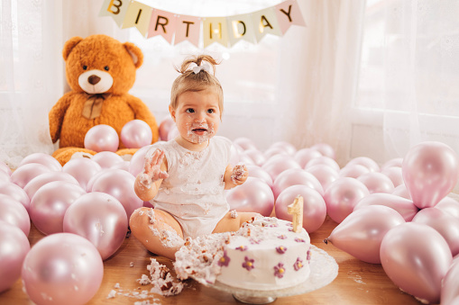 The adorable nervous little girl is eating the cake with her hands on the floor. The child is smashing her birthday cake, but doesn't want to get her hands dirty.