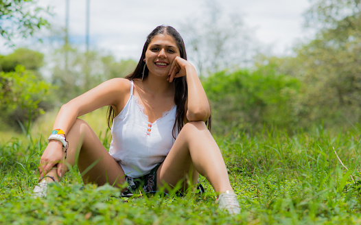 portrait of a woman sitting in a meadow in the open air and smiling with one hand next to her face