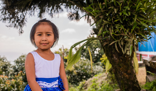 portrait of indigenous girl with short hair taking a walk in the park while wearing a dress and looking at the camera with a smile on her face