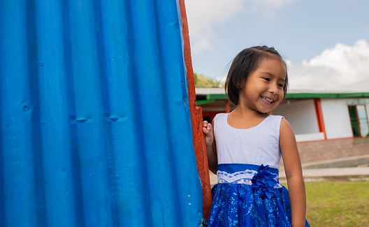 Indian school girl wearing a dress and strolling in the courtyard of her house smiling happily and looking to the side.