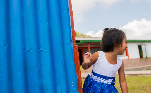 short-haired indigenous girl playing in the courtyard of her house smiling happily looking to the side and wearing a blue dress