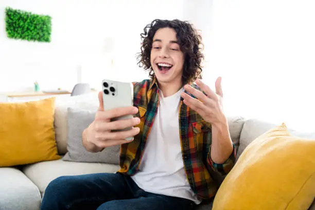 Photo of excited funky guy dressed checkered shirt communicating apple iphone samsung modern gadget indoors house home room.