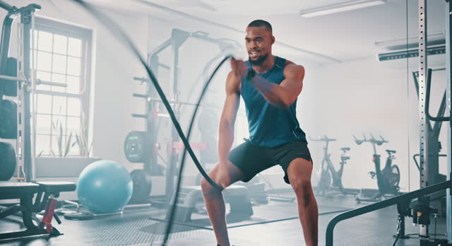 Gym, fitness and black man with battle rope wave for muscle growth, strength development and power exercise. Equipment, endurance and African bodybuilder resilience in workout, challenge or hard work
