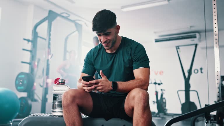 Gym, phone or relax man reading online workout information, training instruction or fitness blog. Cellphone, mobile app and athlete check social media post on challenge, exercise or physical activity